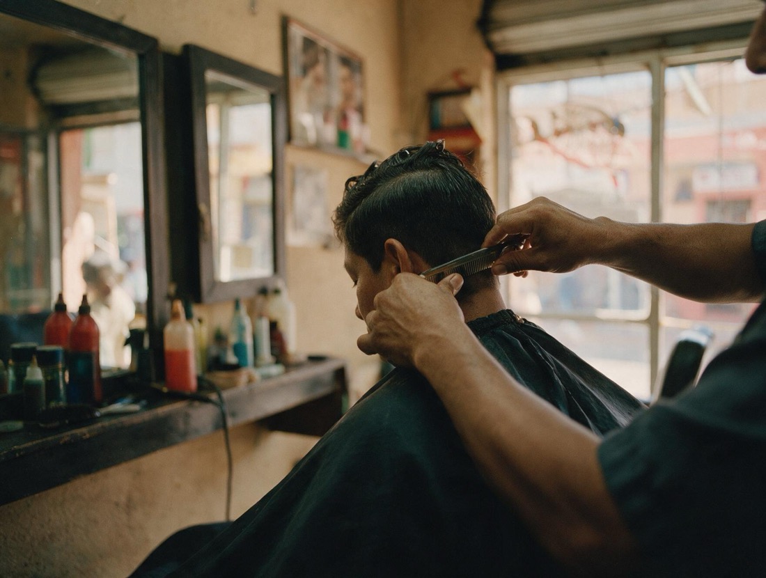 Barbero cortando el cabello a un cliente frente al espejo.